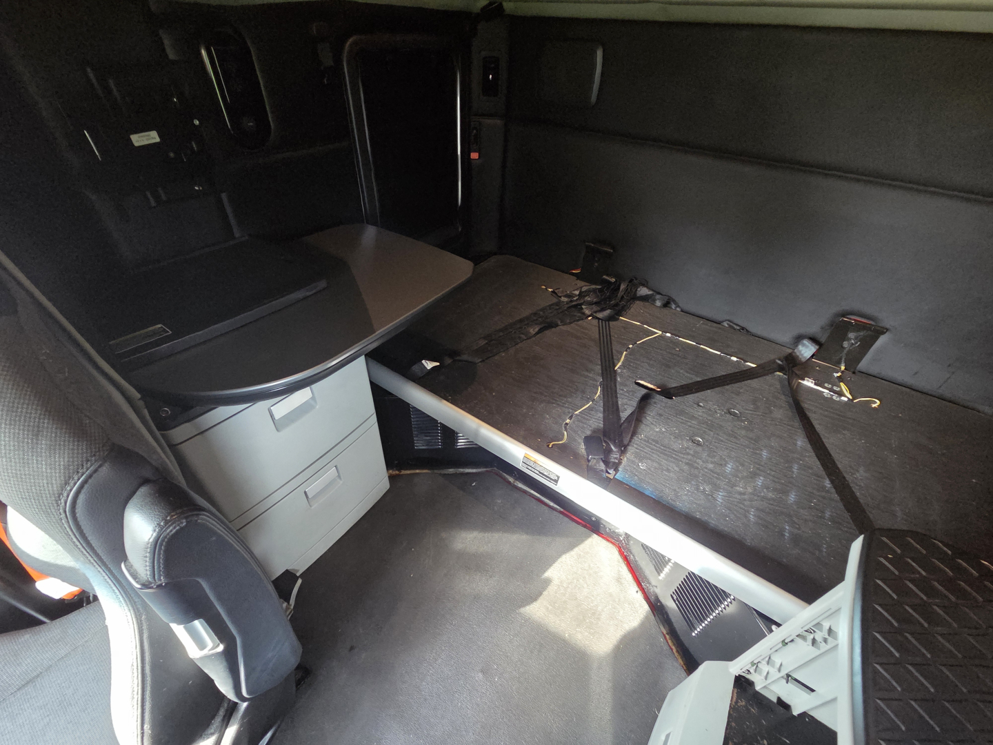 Kenworth T680 sleeper cab interior showing a foldable bed with seat/console area and storage drawers.