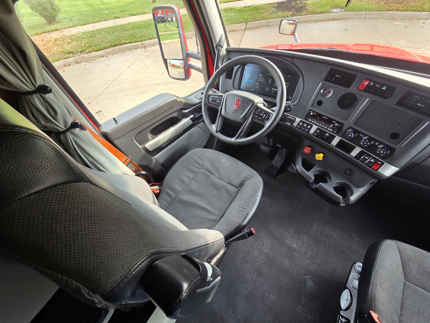 Kenworth T680 interior driver’s seat and dashboard with steering wheel, instrument cluster, center console, and gear shifter.