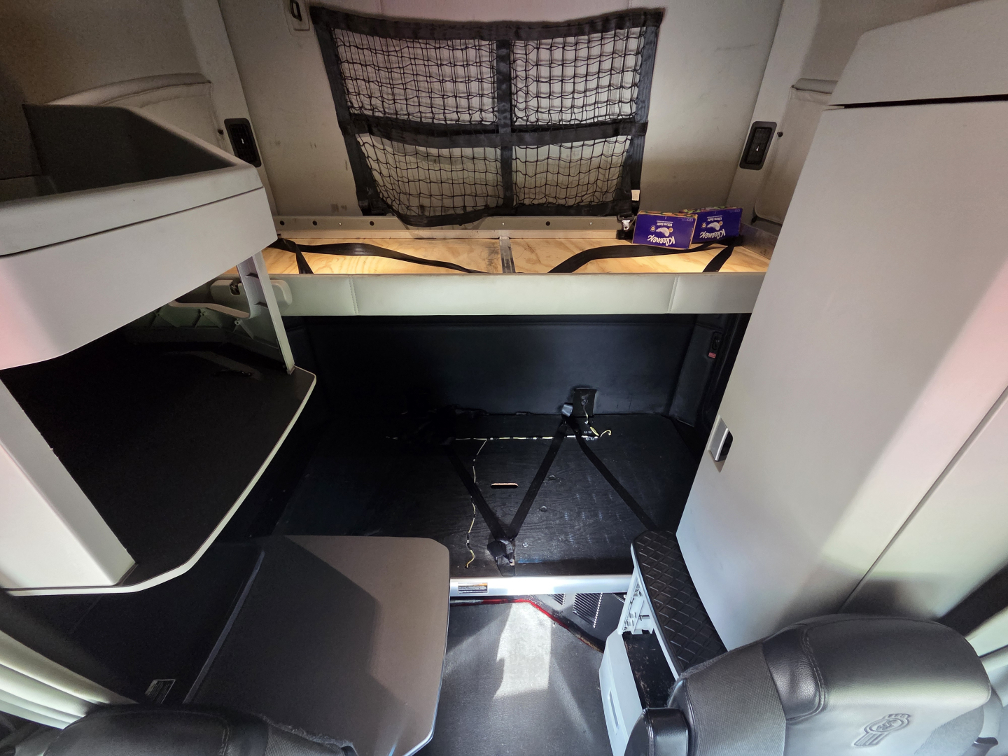 Cab interior of a 2022 Kenworth T680 truck showing the sleeper area and storage compartments, nets, and a visible jack in the floor.