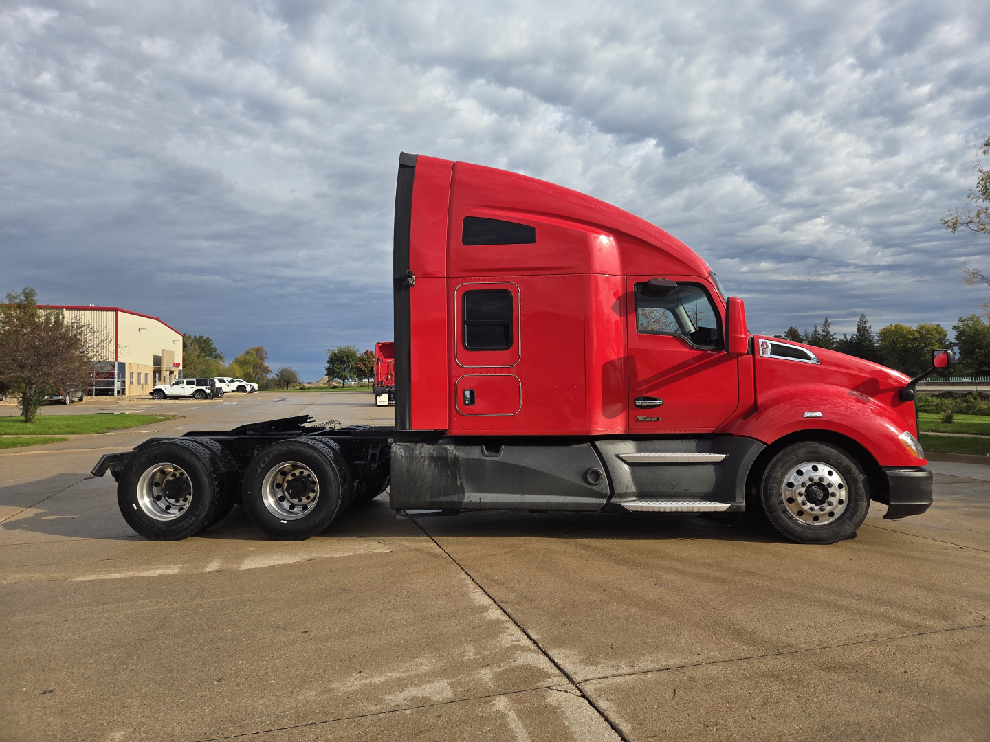 Kenworth T680 sleeper cab truck side view showing red exterior, long hood, dual rear axles, and chrome wheels.