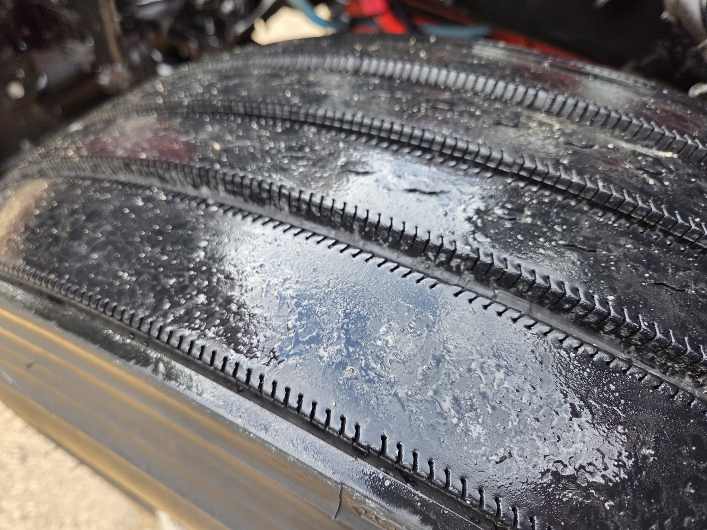 Tire tread close-up on Kenworth T680 undercarriage showing wet road grime and tire grooves.