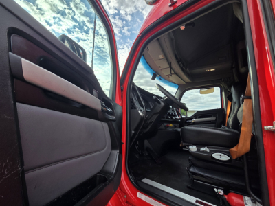 Kenworth T680 truck cab interior view from open driver door showing steering wheel, dashboard, and seat.