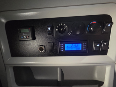 Dashboard panel of a Kenworth truck showing controls and a blue digital display. Visible text on a blue-lit screen and knobs.