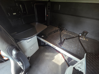Kenworth T680 sleeper cab interior showing a foldable bed with seat/console area and storage drawers.