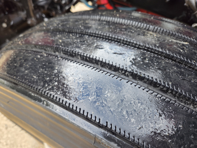 Tire tread close-up on Kenworth T680 undercarriage showing wet road grime and tire grooves.