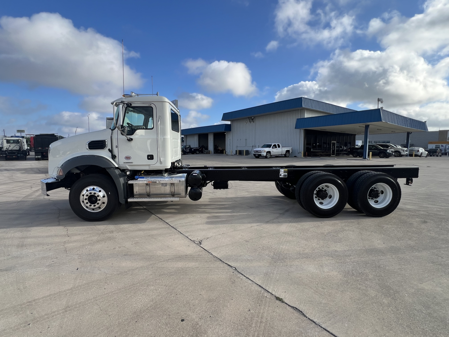 Mack GR64B cab and chassis truck side view showing white cab, long flatbed with dual rear axles, and chrome fuel tanks.