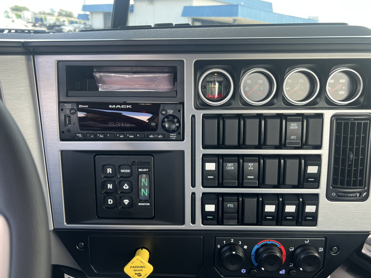 Mack GR64B cab interior dashboard showing gauge cluster, radio, and control switches with gear selector and various buttons.