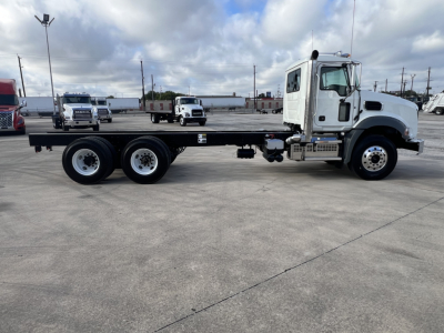Mack GR64B cab and chassis truck side view showing flatbed with long wheelbase and dual rear axles; white cab, gray chassis, parking lot background.