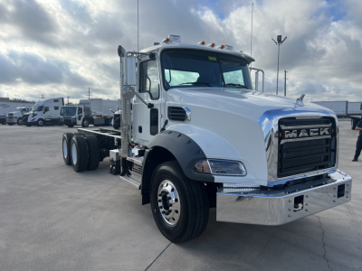 Front-left view of a white 2026 Mack GR64B cab and chassis truck showing chrome bumper, large grille, side exhaust, and dual rear axles.