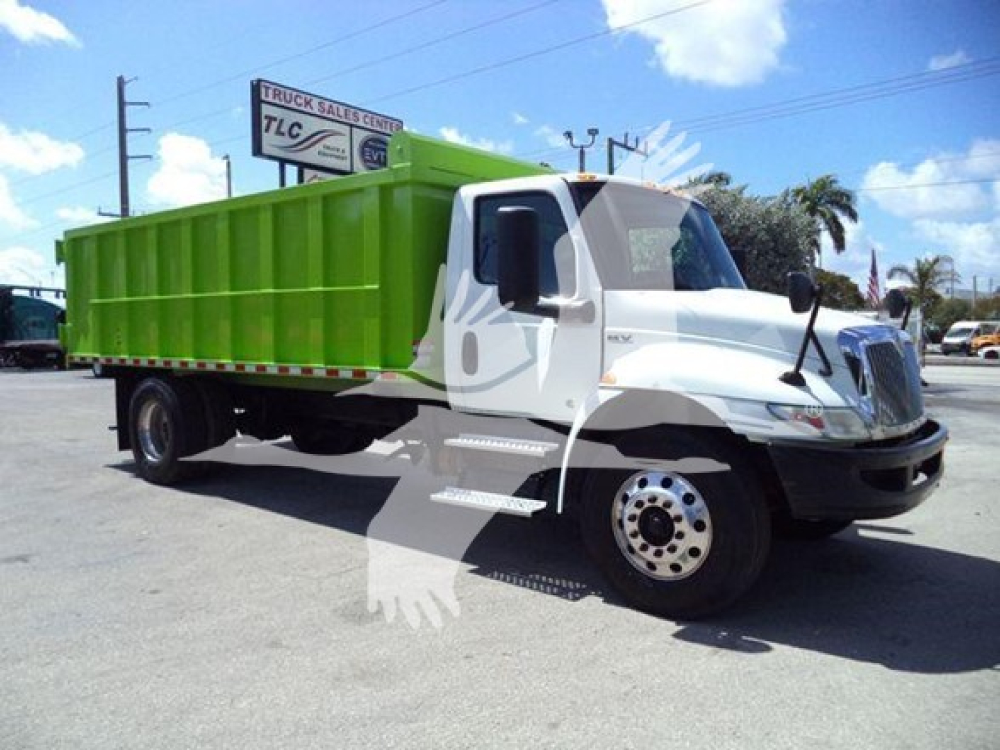 Dump truck showing white cab and bright green dump body with TLC sign in background.