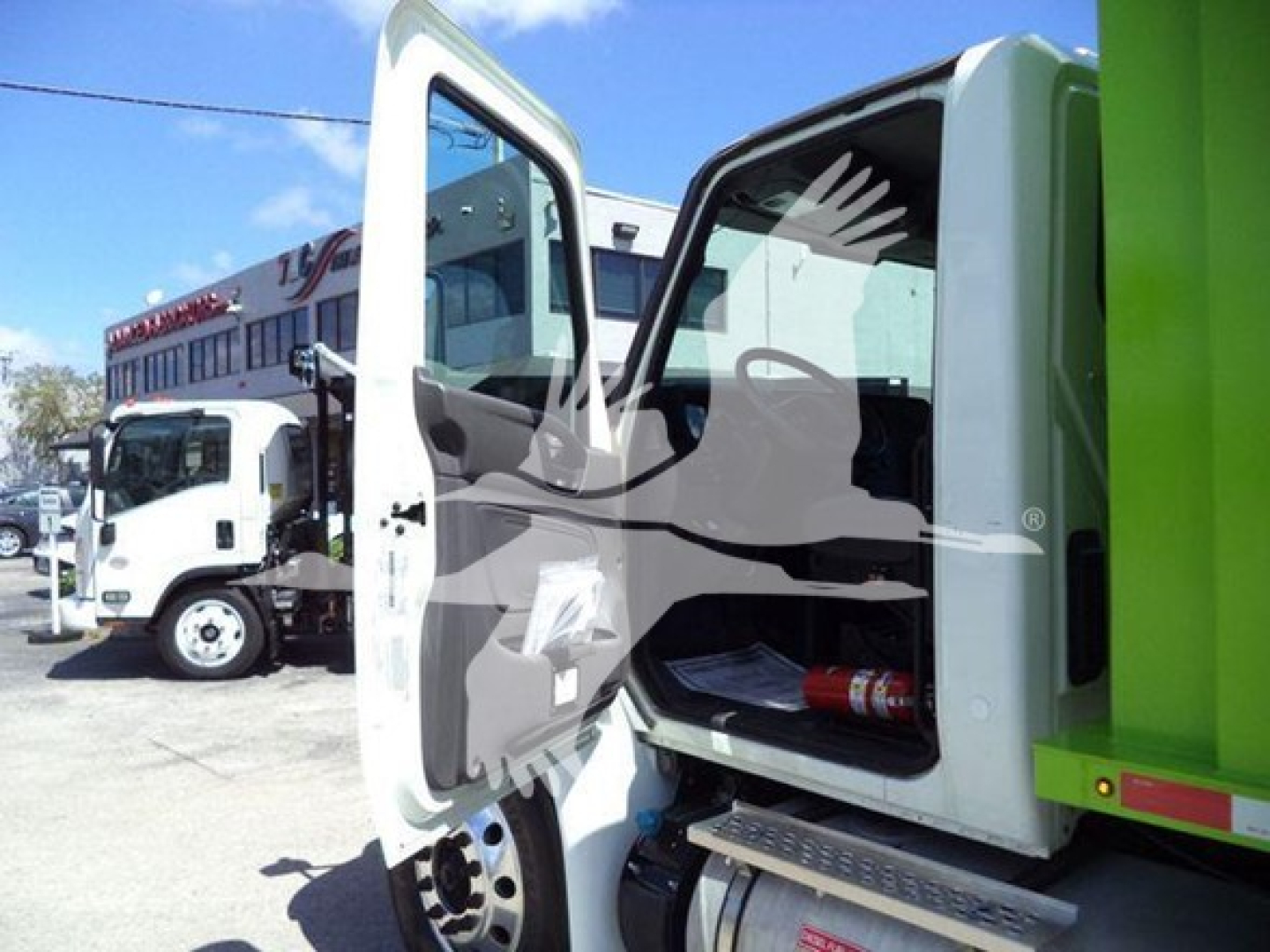 Truck cab interior visible with open door; glimpse of dashboard and storage; other trucks in background.