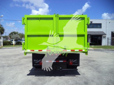 Back view of a bright green dump truck body with tailgate doors, in a parking lot. Brand decals on the black chassis mudflaps.