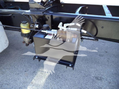 Diesel truck chassis with a mounted auxiliary fuel or fluid transfer tank and hoses under a dump truck frame.