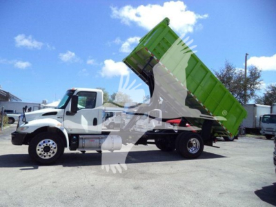 Dump truck with green dump bed raised on a white International MV chassis, side view showing cab, wheels, and hydraulic raise arm.