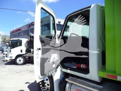 Truck cab interior visible with open door; glimpse of dashboard and storage; other trucks in background.
