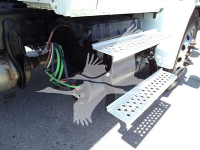Truck cab area showing under-ride air filter housing and exposed wiring near steps and fuel tank; metal perforated steps visible.