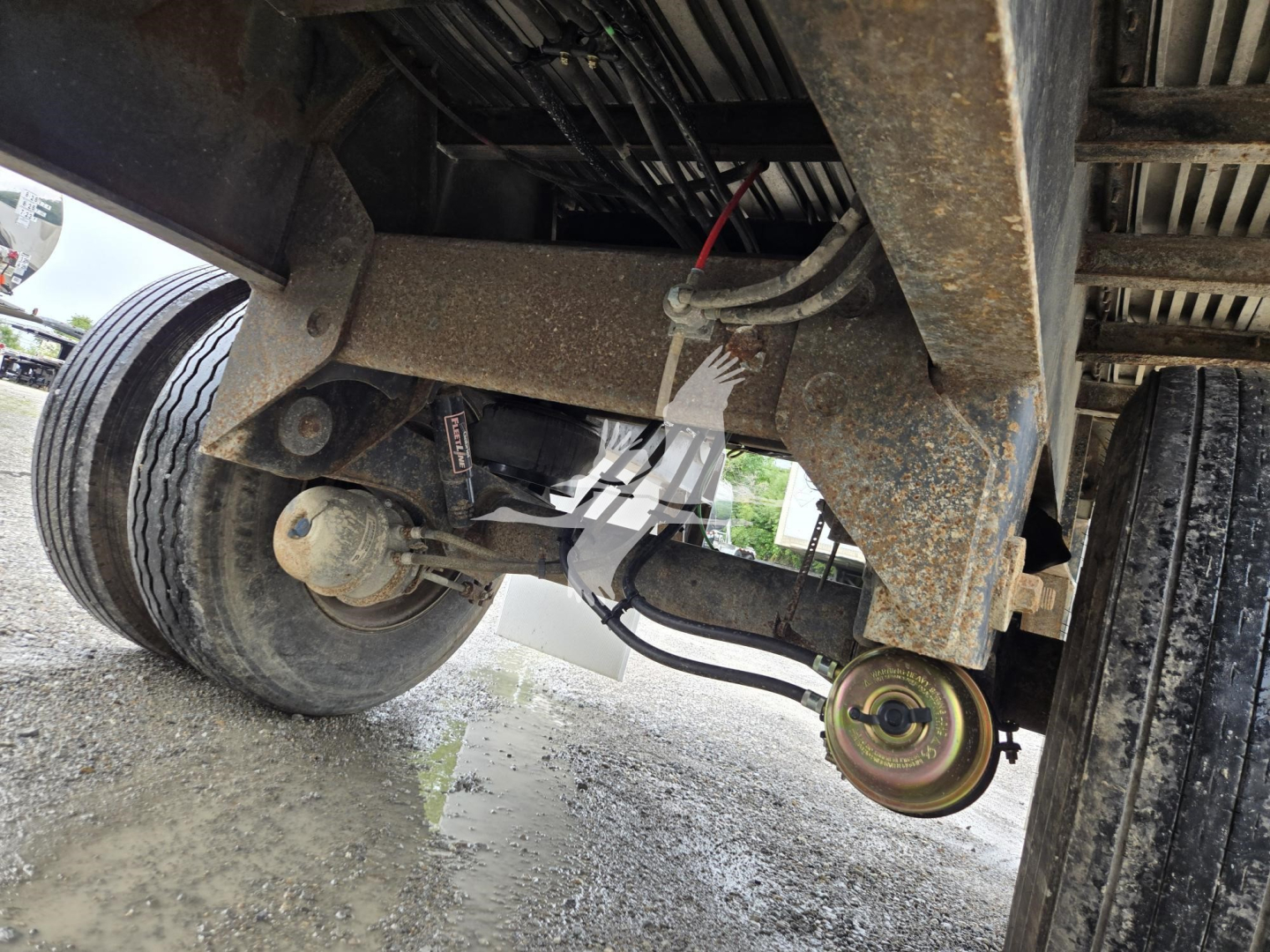 Trailer undercarriage view of a 2016 Utility Combo Flatbed showing suspension components, leaf springs, axles, and a yellowish wheel hub. Visible hoses and wiring.