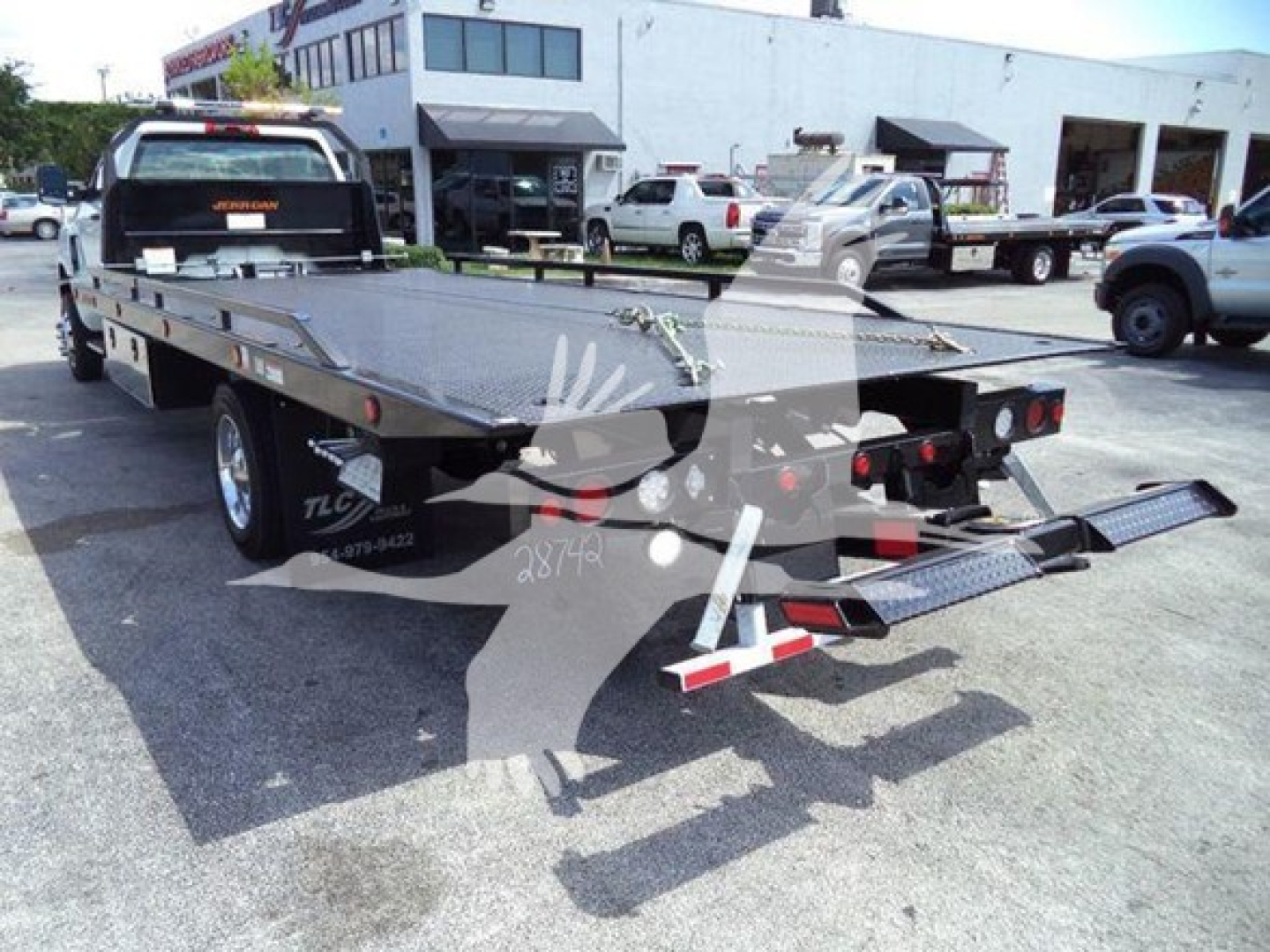 Flatbed tow truck trailer showing ramp at rear and platform inlay with hydraulic hoses and taillights.