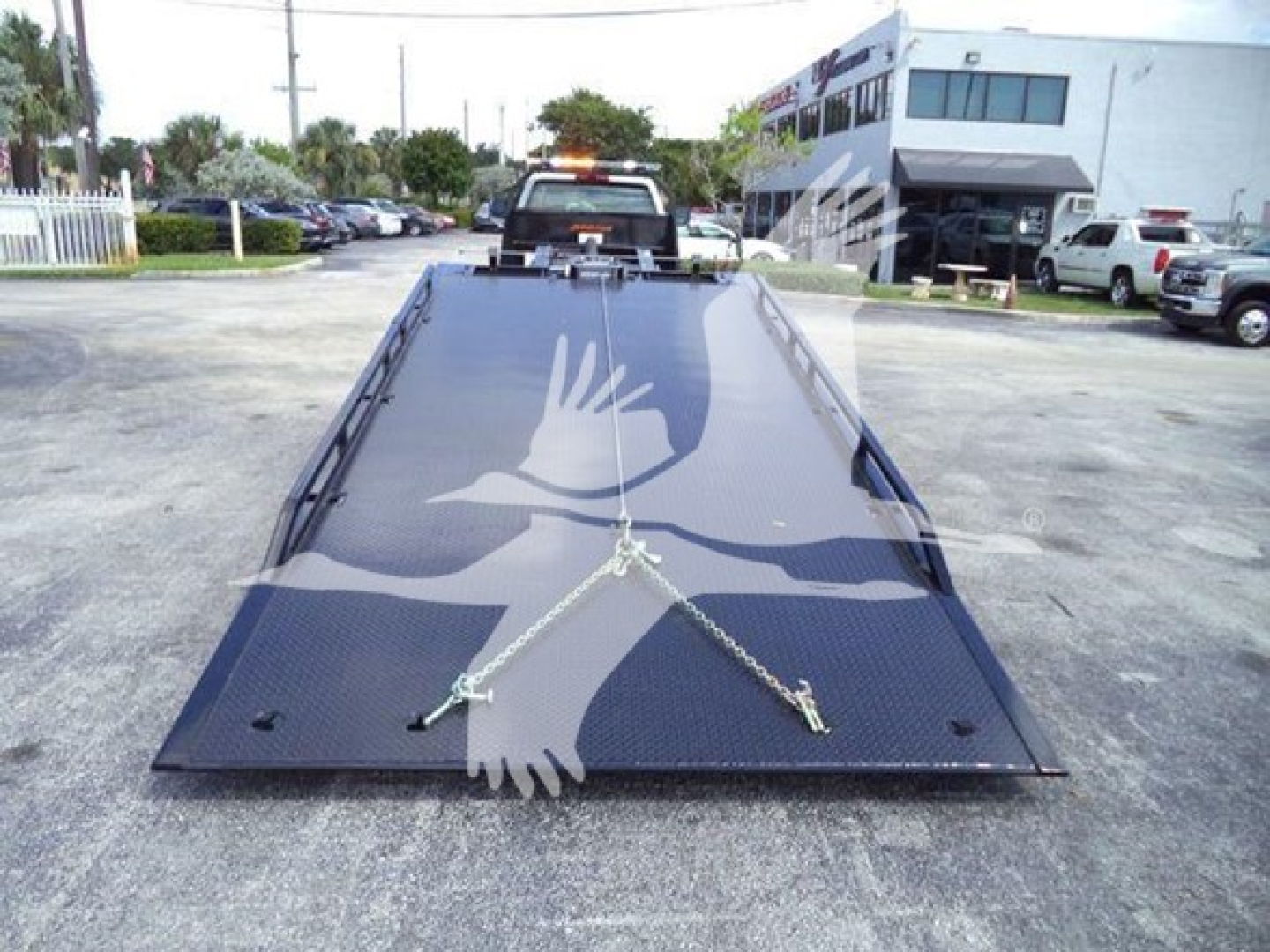 Tow truck flatbed with wheel-lift setup and chain ties on a black metal incline in a dealership lot.