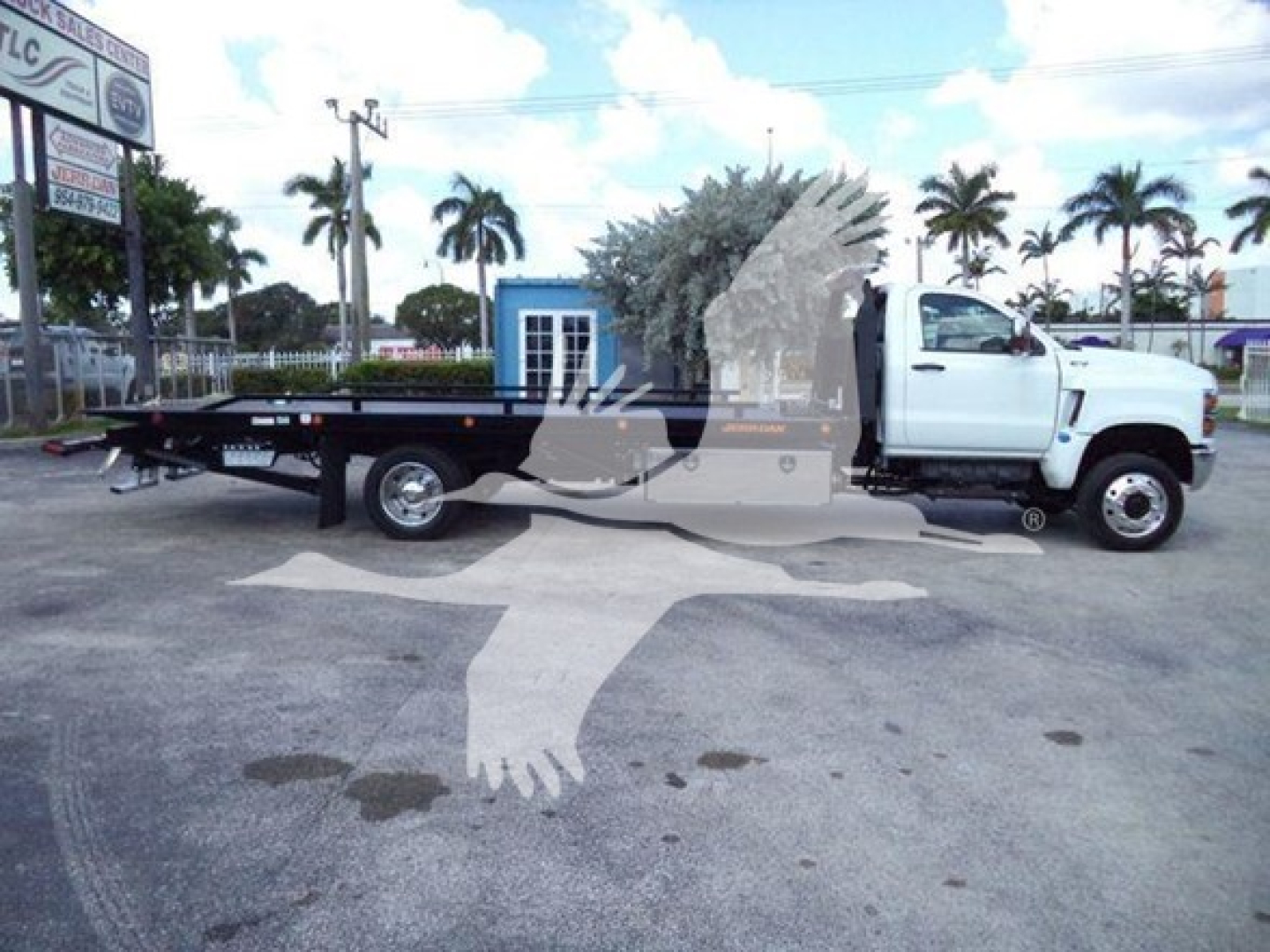 White International CV rollback truck with flatbed on a lot, VIN 1HTKTSWK2PH441633 visible on listing; palm trees in background.