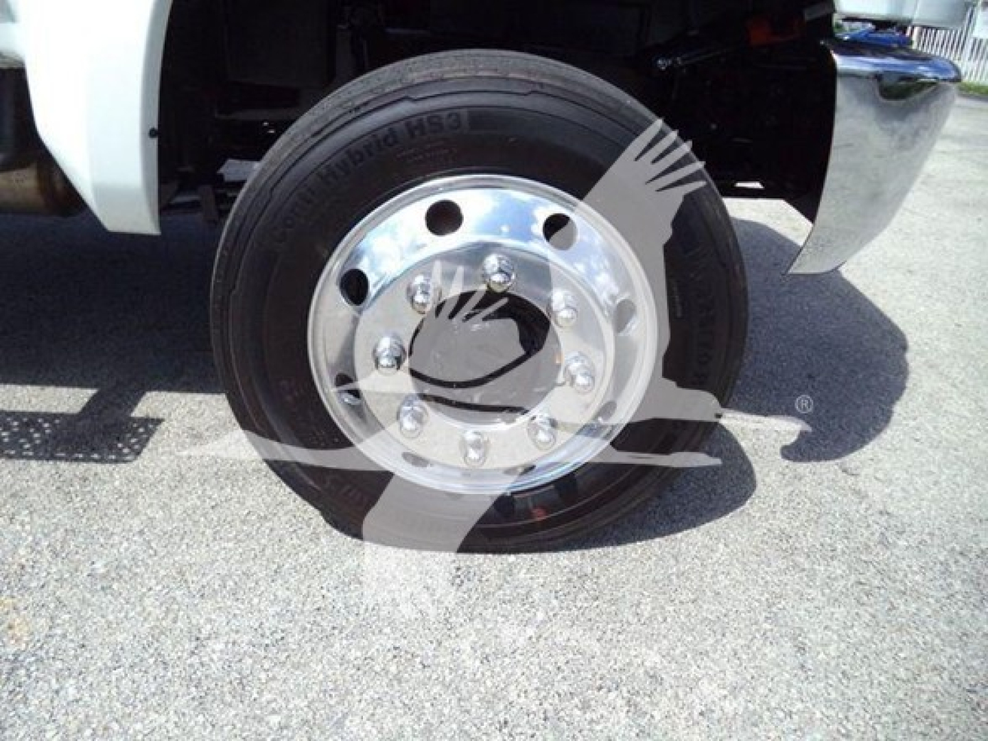 Truck wheel and tire on a white International CV Series chassis showing a mounted hubcap and Michelin tire with clear sidewall lettering, partial front fender and paved ground.