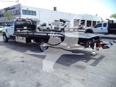 Flatbed rollback truck with a long black bed and调整 gooseneck in a dealership lot.