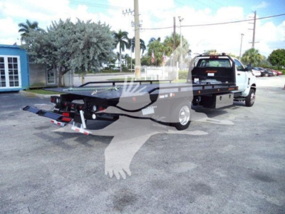 Flatbed tow truck in a dealership lot showing rear and long wheelbase, with hitch and ramps visible.