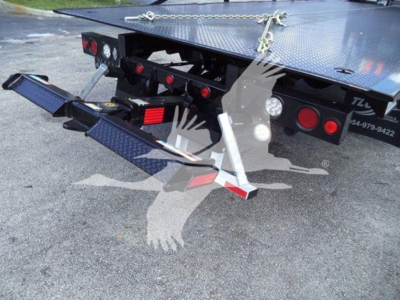 Truck rollback bed with rear ramps extended showing tail lights, chains, and reflective triangle on black metal bed.