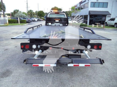 Tow truck rollback bed with metal platform and rear lights, rear view showing hydraulic components and safety rails.