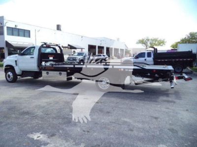 Tow truck flatbed rollback with white cab and long black bed, VIN label visible on side, in a dealership lot.