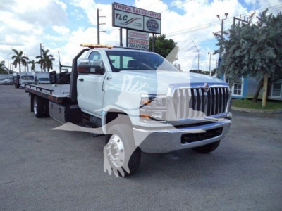 Truck bed rollback wrecker chassis on white International CV towing truck, front grille, large side mirrors, dealership lot background.