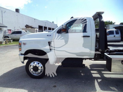 Truck side view showing white 2023 International CV rollback tow truck with EV badge and chrome wheel, cab door, black chassis, and rear ramp.