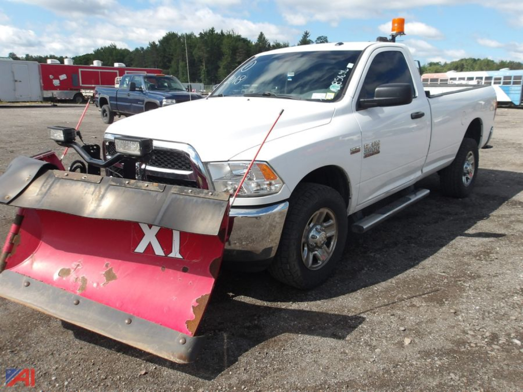 Ram pickup truck with plow attached, white 2018 model, 4x4, front view showing plow and amber beacon on cab.