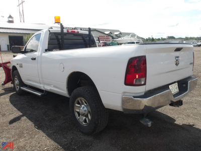 Ram 2500 pickup two-tone white truck with plow mount at rear and roof beacon, side steps, and tow hitch visible in a gravel lot.