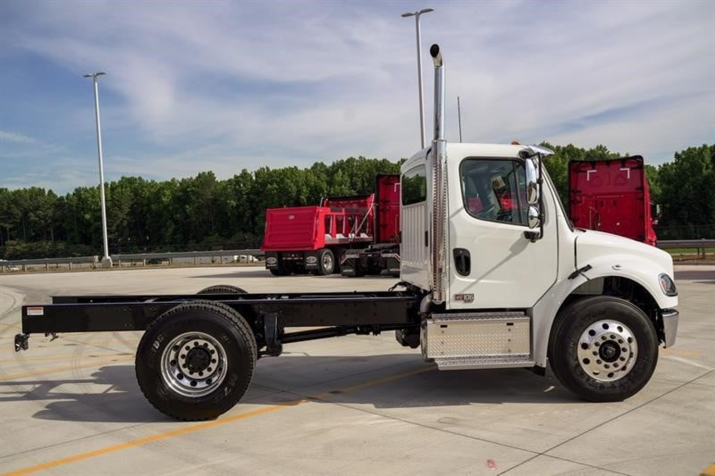 Freightliner M2 106 Plus chassis cab side view showing long flatbed frame and white cab.