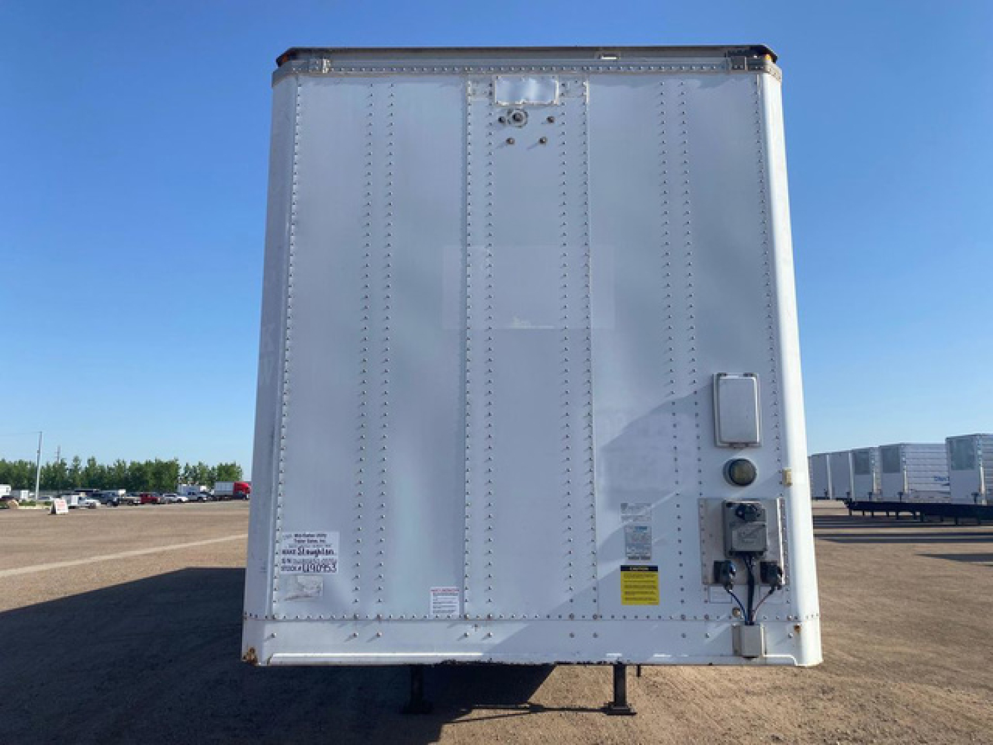 Rear view of a white Stoughton van trailer showing riveted metal panels, a rear bumper, and electrical/air connections on the right side with safety decals.