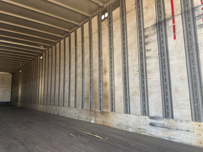 Trailer interior showing metal wall rails and wood floor with marks; no readable branding or numbers visible.