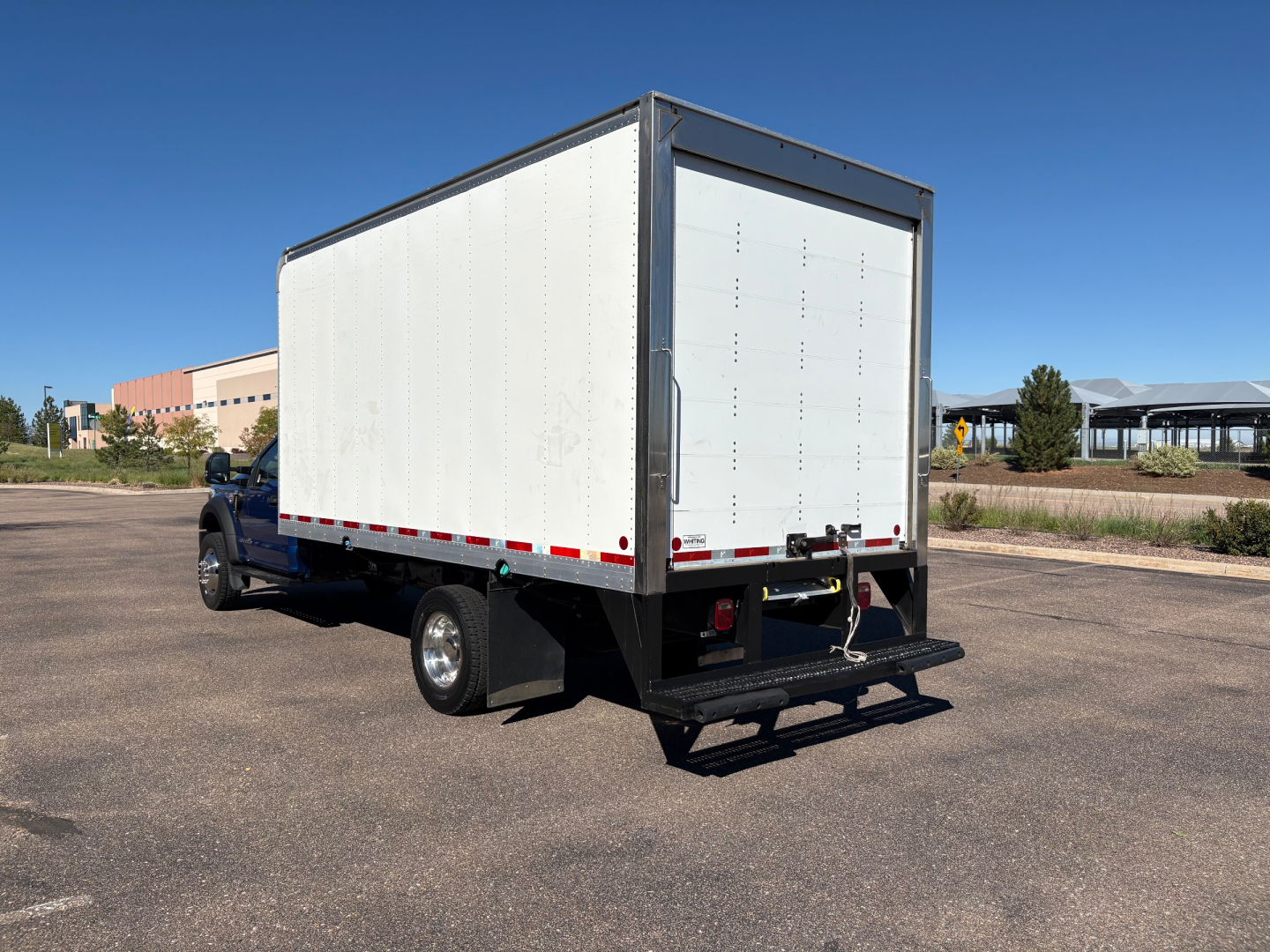 Ford F-550 box truck rear view showing a large white cargo box with black framing and a fold-down bumper step.
