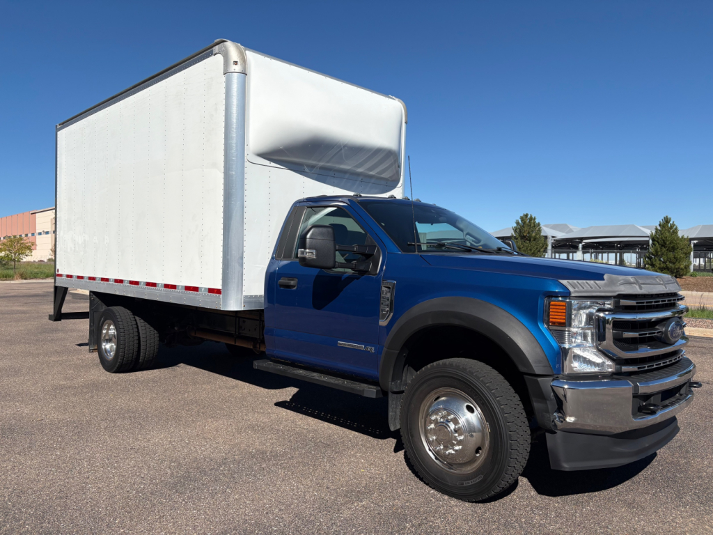 Ford F-550 box truck in blue cab with a large white box, side view showing front grille, wheel, and cargo box.