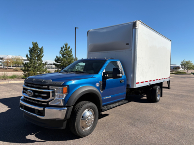 Ford F-550 box truck in blue cab and white cargo box, front and side view, clear sky.