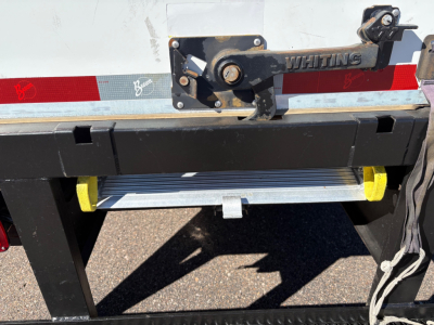 Rear view of a box truck cargo area showing Whiting latch, reflective tape, and a metallic step/bumper with yellow ends.