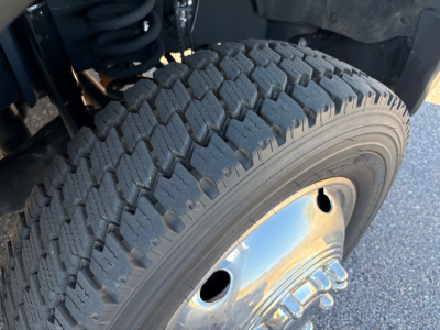 Ford F-550 wheel and tire showing off-road tread and chrome hubcap, front left suspension components visible