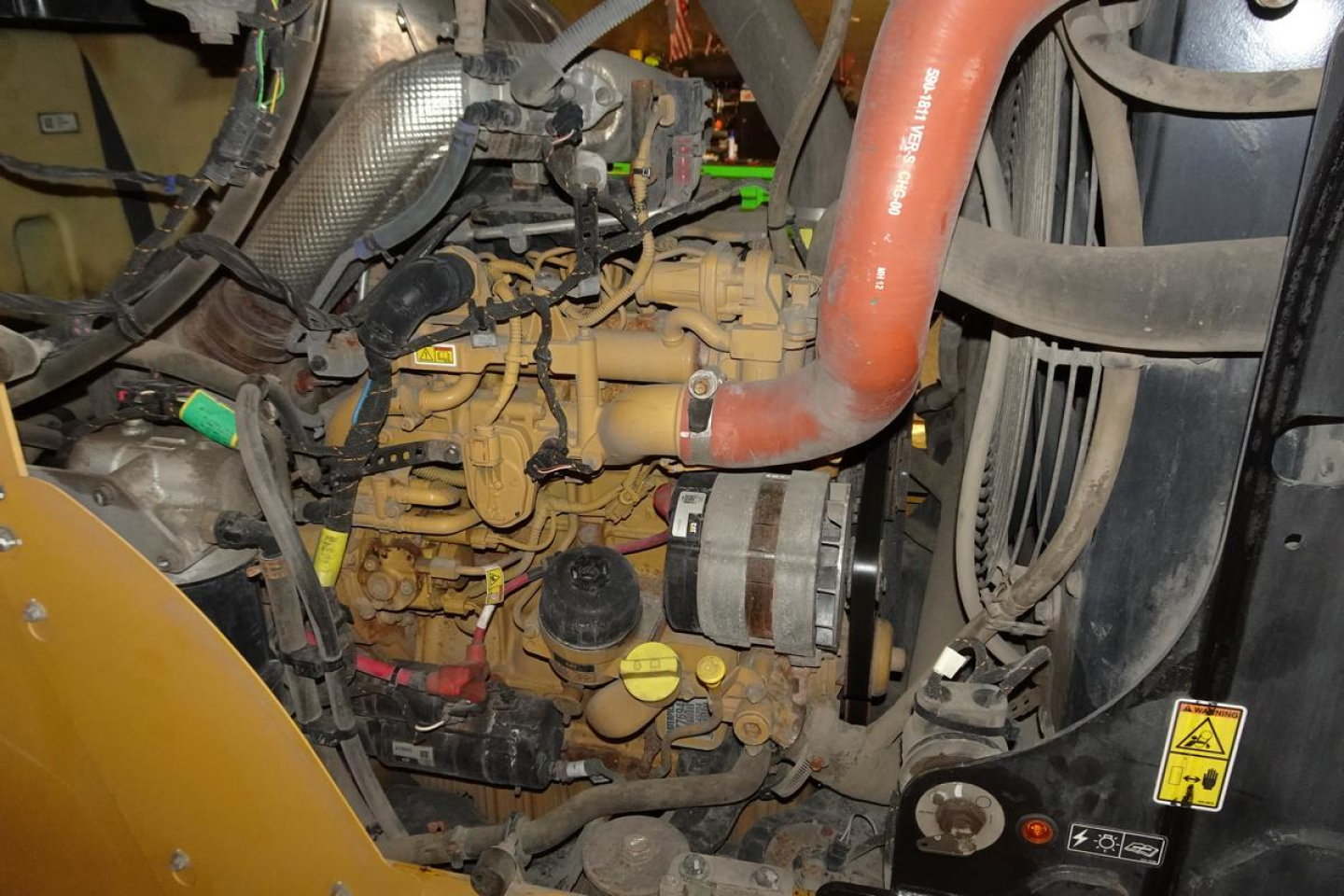 Caterpillar 914 wheel loader engine bay showing yellow engine block, orange coolant hose, black circular dipstick, and radiator area with warning sticker.