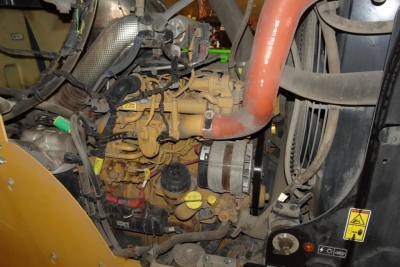Caterpillar 914 wheel loader engine bay showing yellow engine block, orange coolant hose, black circular dipstick, and radiator area with warning sticker.