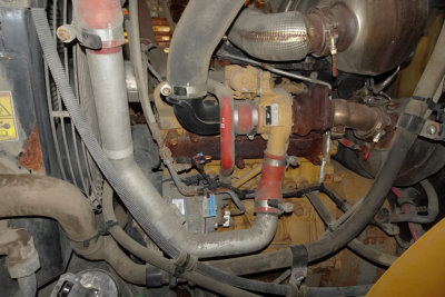 Caterpillar 914 engine bay showing exhaust manifold, hoses, and various red and yellow coolant/fluids lines.