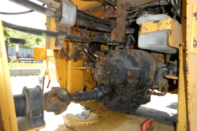 Caterpillar 914 wheel loader drivetrain area showing differential/hub assembly with hydraulic lines and rusted components, inside yellow equipment frame.