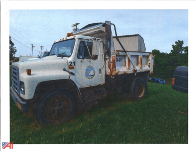 Dump truck from 1986 International 1954 Cab showing a white cab and dump bed with logo on door and platform for hauling material.