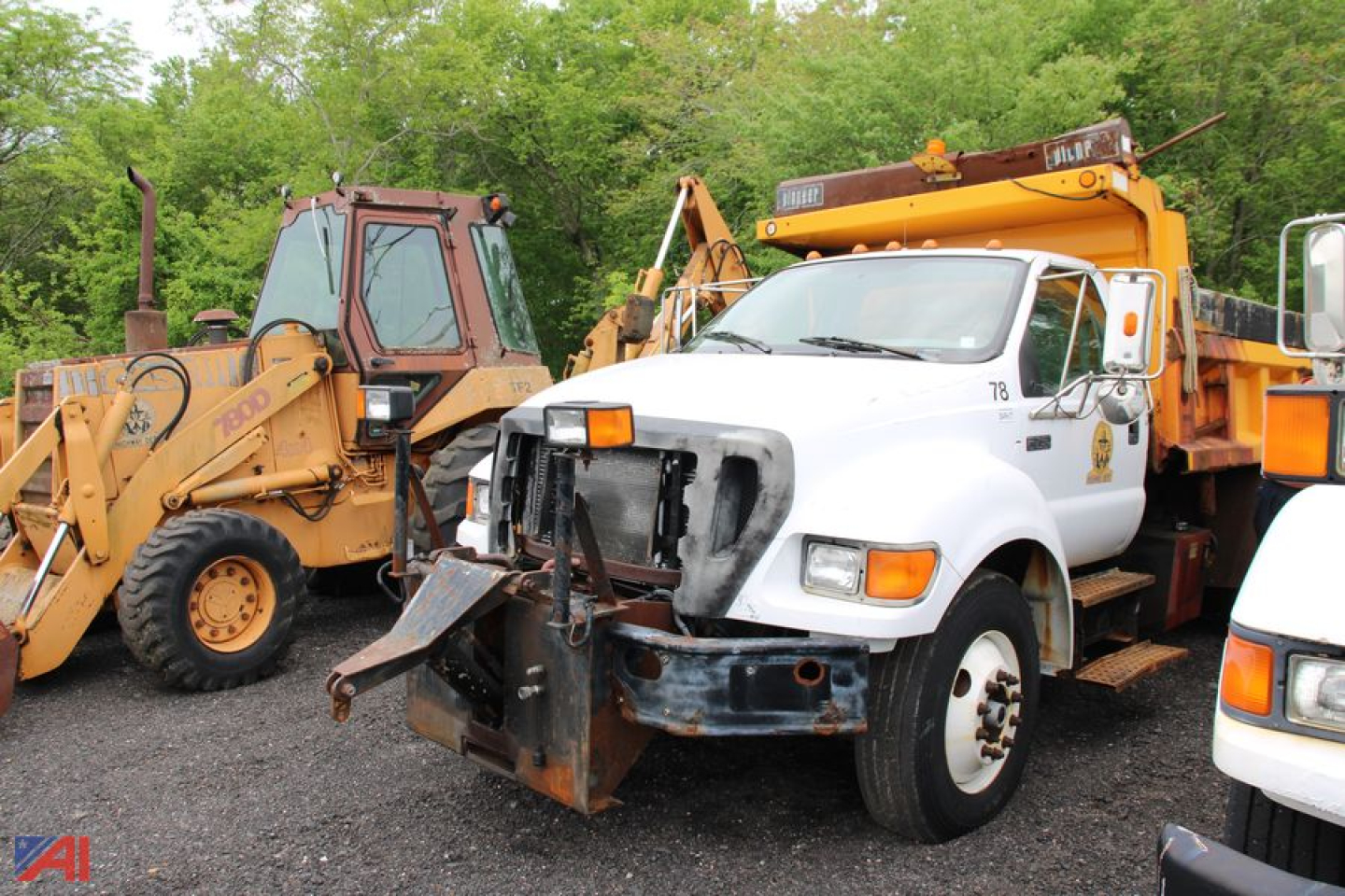 Side view of a white Ford F-750 Super Duty dump truck with front bumper guard and equipment on a loader yard, surrounded by yellow construction machinery.