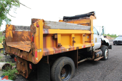 Ford F-750 dump truck side rear view showing dump bed and dual rear wheels with orange body and black chassis