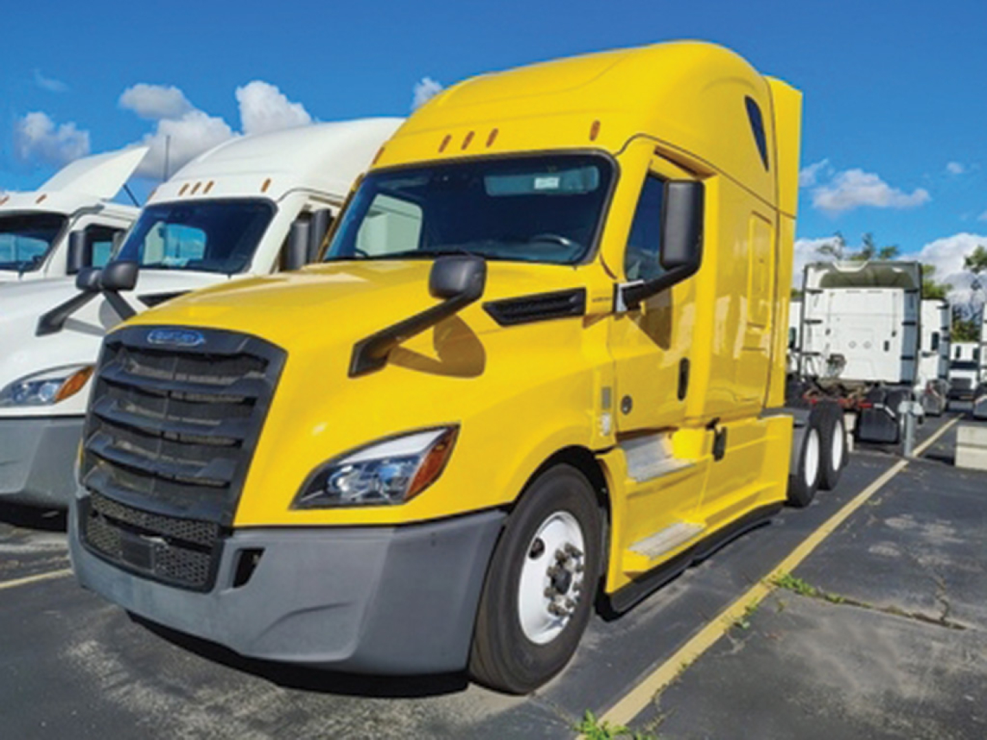 Truck image of a bright yellow Freightliner Cascadia126 sleeper tractor in a parking lot showing the front grille and cab doors.